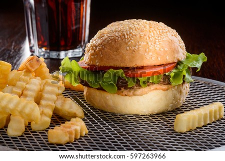 The dinner is served. This picture could make you hungry: a tasty burger with beef and vegetables, french fries scattered over a gridded silver tray and a glass of cola to wash it all down.