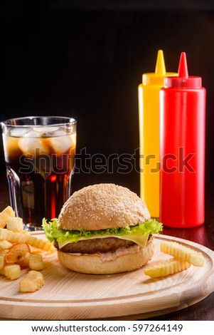 Vertical shot of a meal. Light wooden tray with delicious cheeseburger and french fries, a glass of cola and two sauce bottles over dark background. Mouth-watering picture of fast food.