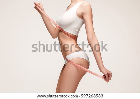 The girl taking measurements of her body, white background. Royalty-Free Stock Photo #597268583