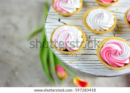 Tartlets with merengue, cream white on a stand with flowers on a gray table
