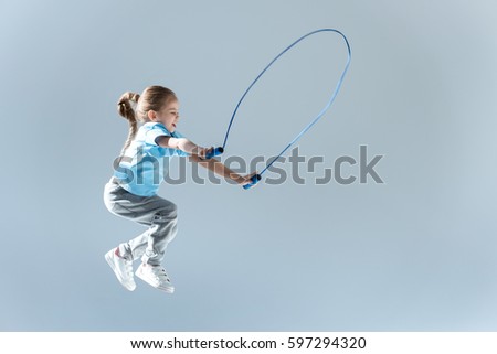 side view of happy girl humping exercising with skipping rope isolated on grey Royalty-Free Stock Photo #597294320