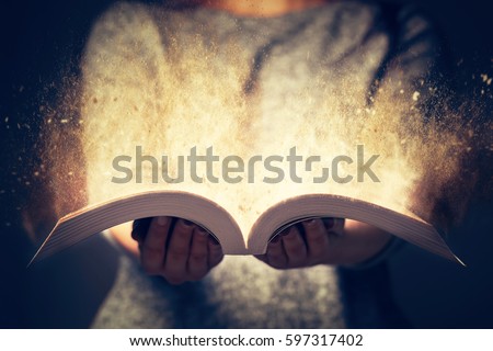 Woman holding an open book with two hands. Light coming out of the book as a concept of learning, education, knowledge and religion Royalty-Free Stock Photo #597317402