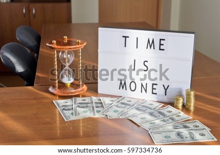 'Time is money' letters shown in lightbox put on the desk in office interior.