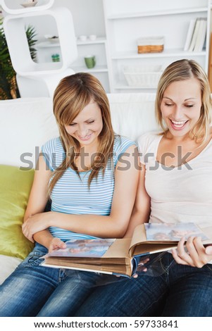 Two charming female friends looking at a photo album together on a sofa at home