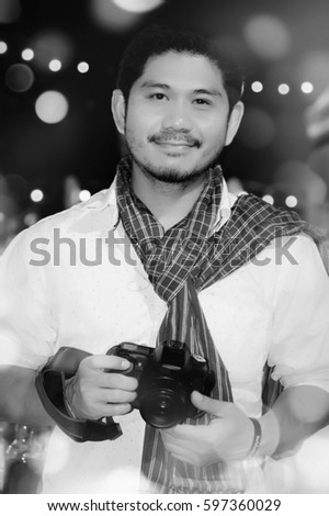 Black&white Portrait of a happy photographer man holding camera while expressing smile with bokeh background