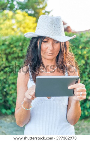 Beautiful woman dressed in white outdoor using tablet.