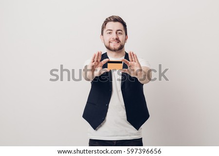 young handsome man with beard in white shirt and black waistcoat holding plastic credit card and smiling. focus on card. soft light