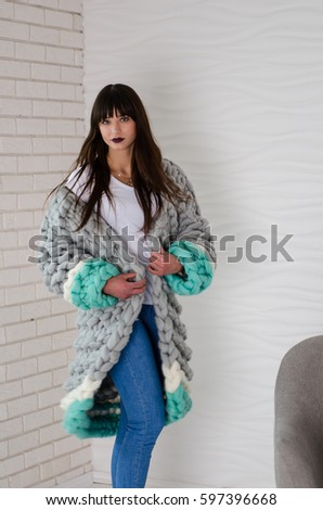 Young beautiful fashionable woman standing near chair in merino wool jacket