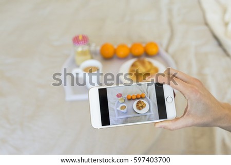 woman taking picture of  tray with breakfast on her smart phone. Top view. Lifestyle