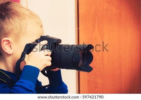 Child passion and hobbies concept. Kid playing with big professional digital camera, photographing various things in house