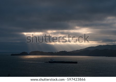 The shadow of a gas tanker entering the port of San Francisco with sun rays through the clouds in the background, USA.