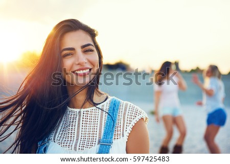 Summer scene of smiling woman with pair of dancing friends in background on beach during sunset