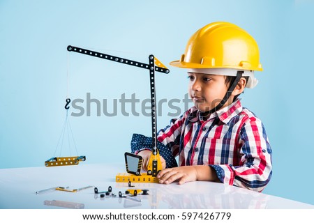 Cute little indian boy playing with toy crane wearing yellow construction hat or hard hat, childhood and education concept