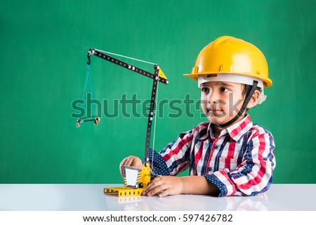 Cute little indian boy playing with toy crane wearing yellow construction hat or hard hat, childhood and education concept, isolated over green chalkboard