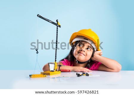 cute indian baby girl playing with toy crane wearing yellow construction hat or hard hat, childhood and education concept