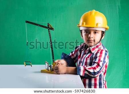 Cute little indian boy playing with toy crane wearing yellow construction hat or hard hat, childhood and education concept, isolated over green chalkboard