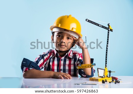 Cute little indian boy playing with toy crane wearing yellow construction hat or hard hat, childhood and education concept