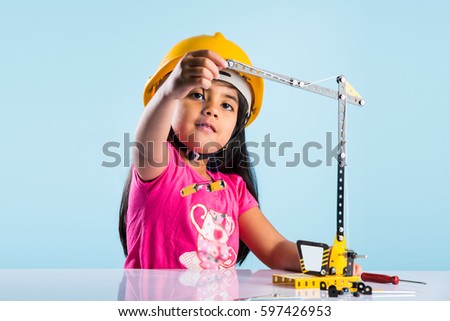 cute little indian baby girl playing with toy crane wearing yellow construction or hard hat, childhood and education concept