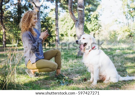 Young female taking photo of labrador retriever dog in park