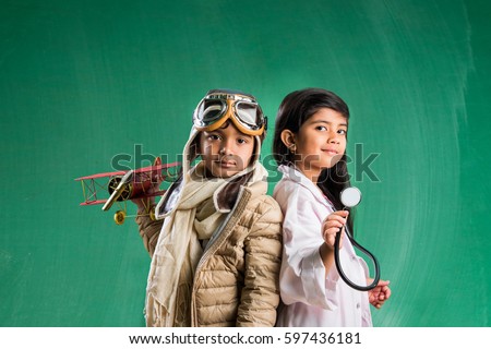 Kids and education concept - Small indian boy and girl posing in front of Green chalk board in pilot fancy dress and doctor costume with stethoscope, standing over green chalkboard background Royalty-Free Stock Photo #597436181
