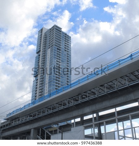 Skyscraper behind bridge under construction. Blue sky and clouds background.