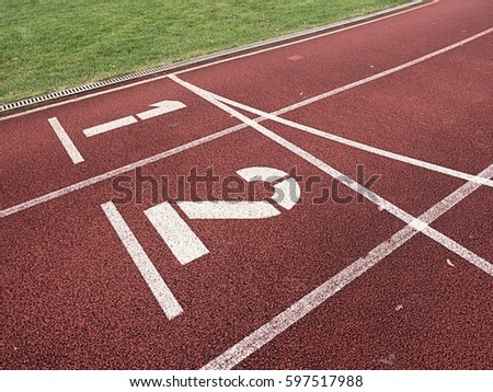 White track number on red rubber racetrack, texture of running racetracks in small stadium. Number one and number two. Outdoor excercise. 