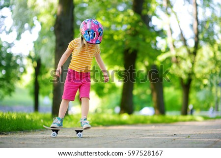 Pretty little girl learning to skateboard on beautiful summer day in a park. Child enjoying skateboarding ride outdoors. 