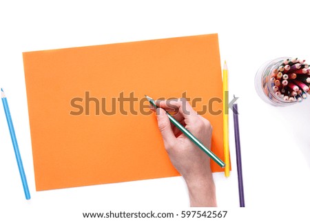 Female hand is ready for drawing with green pencil on orange paper. Isolated on white.