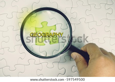 Education concept – a hand holding magnifying glass on white puzzle with a green space.