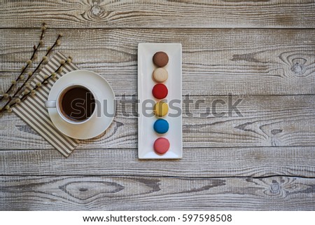 Colorful macaroons with cup of coffee on the napkin on vintage white wooden background.