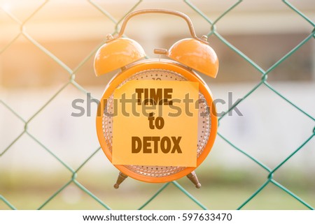 TIME TO DETOX word written on sticky note on orange analog clock hanging on the fence over blurry background Royalty-Free Stock Photo #597633470