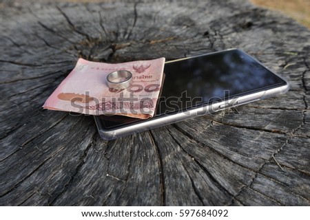 mobile banknote and ring placed on wooden floor
