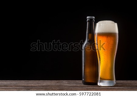 Bottle and glass of beer on a wooden table. Cold malted beverage with large head. Studio shot with black background and copy space to insert your text or picture.