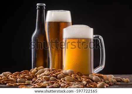 Handful of snack and ale. A bottle, a glass and a mug of fine quality beer surrounded with crunchy pretzels, salty peanuts and pistachios.