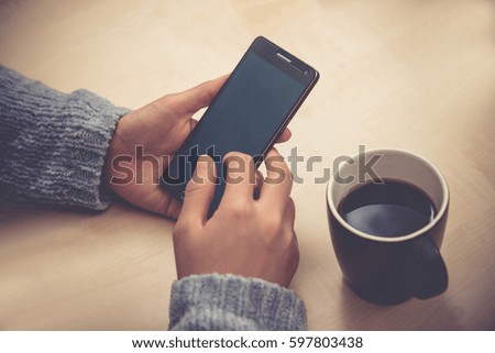Young woman holding mobile phone, a cup of coffee nearly. Social network. Hand focus, Vintage style.
