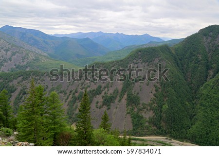 Beautiful summer landscape in the mountains. Top view of mountain forest landscape with giant gray clouds and misty sunlight as a background. Green wood mountain forest in clouds scenery. 