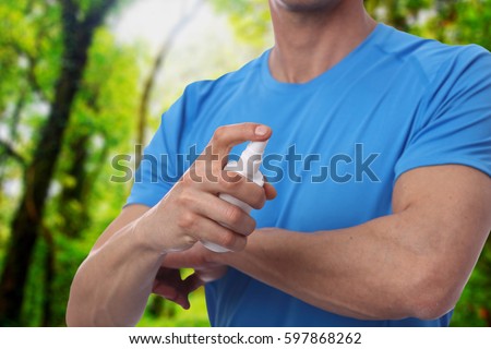Mosquito repellent. Man using insect repellent spray from bottle in forest. Royalty-Free Stock Photo #597868262