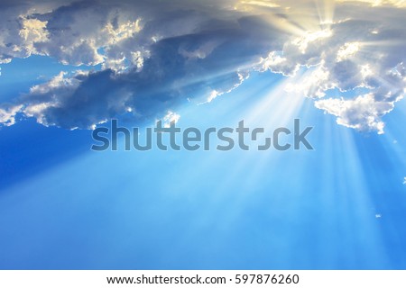 Sun light rays or beams bursting from the clouds on a blue sky. Spiritual religious background. Royalty-Free Stock Photo #597876260