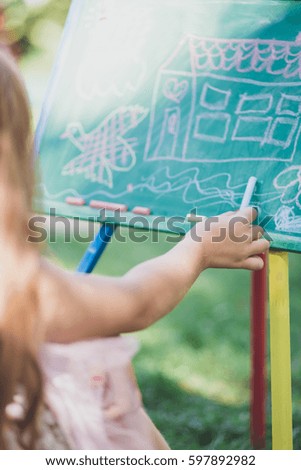 Beautiful girl with red hair preparing for school and writing on blackboard in nature. Selective focus on girl's hand.