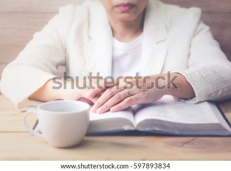 woman is praying on burred open holy bible with a cup of coffee on wooden table
