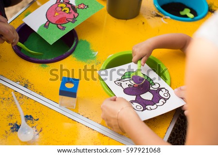 A child draws with colored sand picture. Cartoon characters.