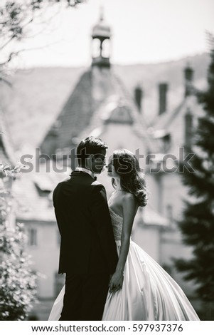 Black and white picture of magnificent wedding couple standing on path to beautiful estate