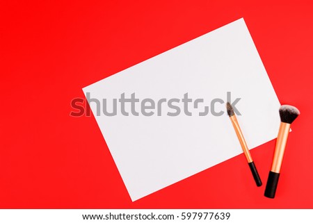 Make up brushes with white blank paper on red background. Top view. Flat lay. Copy space for text