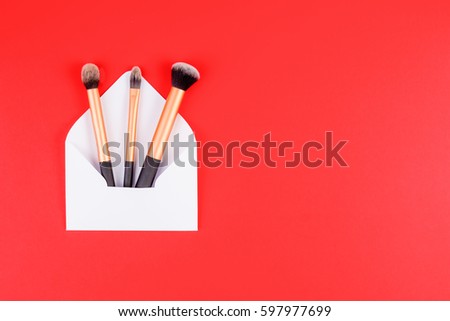 Make up brushes with white open envelope on red background. Top view. Flat lay. Copy space for text