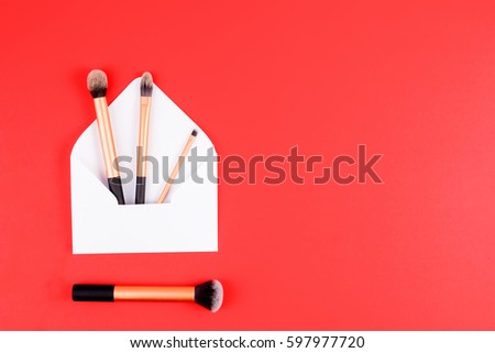 Make up brushes with white open envelope on red background. Top view. Flat lay. Copy space for text