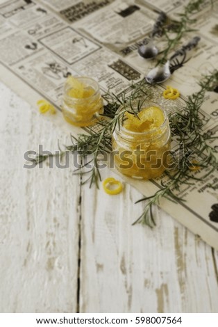 orange marmalade in small glass jars with rosemary on a wooden table and newspaper, selective focus, top view