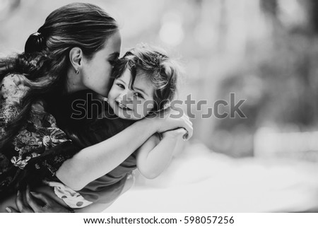 Young woman kisses charming little girl holding her on the arms Royalty-Free Stock Photo #598057256