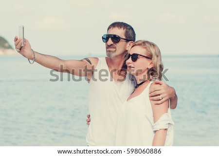 Happy romantic couple embracing on the beach and taking a photo with smart phone. Happy mature couple take a picture.