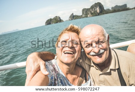 Happy retired senior couple taking travel selfie around world - Active elderly concept with people having fun together at Phang Nga bay Thailand - Mature lifestyle - Retro contrast filter
