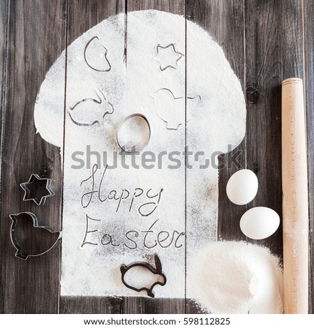 Symbolic image Easter cake with utensils on a dark wooden background. Rolling pin, cookie cutters cutting, eggs, flour